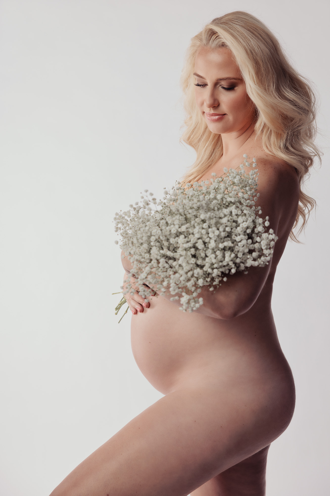 maternity photo of woman holding baby's breath flowers in studio